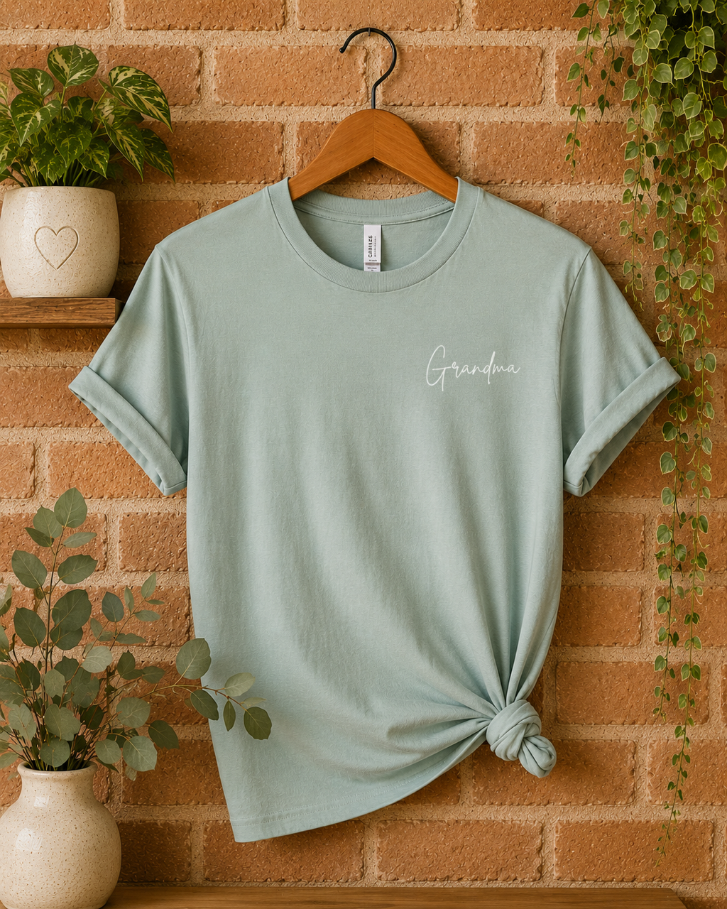 "Grandma" is written in white script on the front left chest on a blue-green soft tshirt.