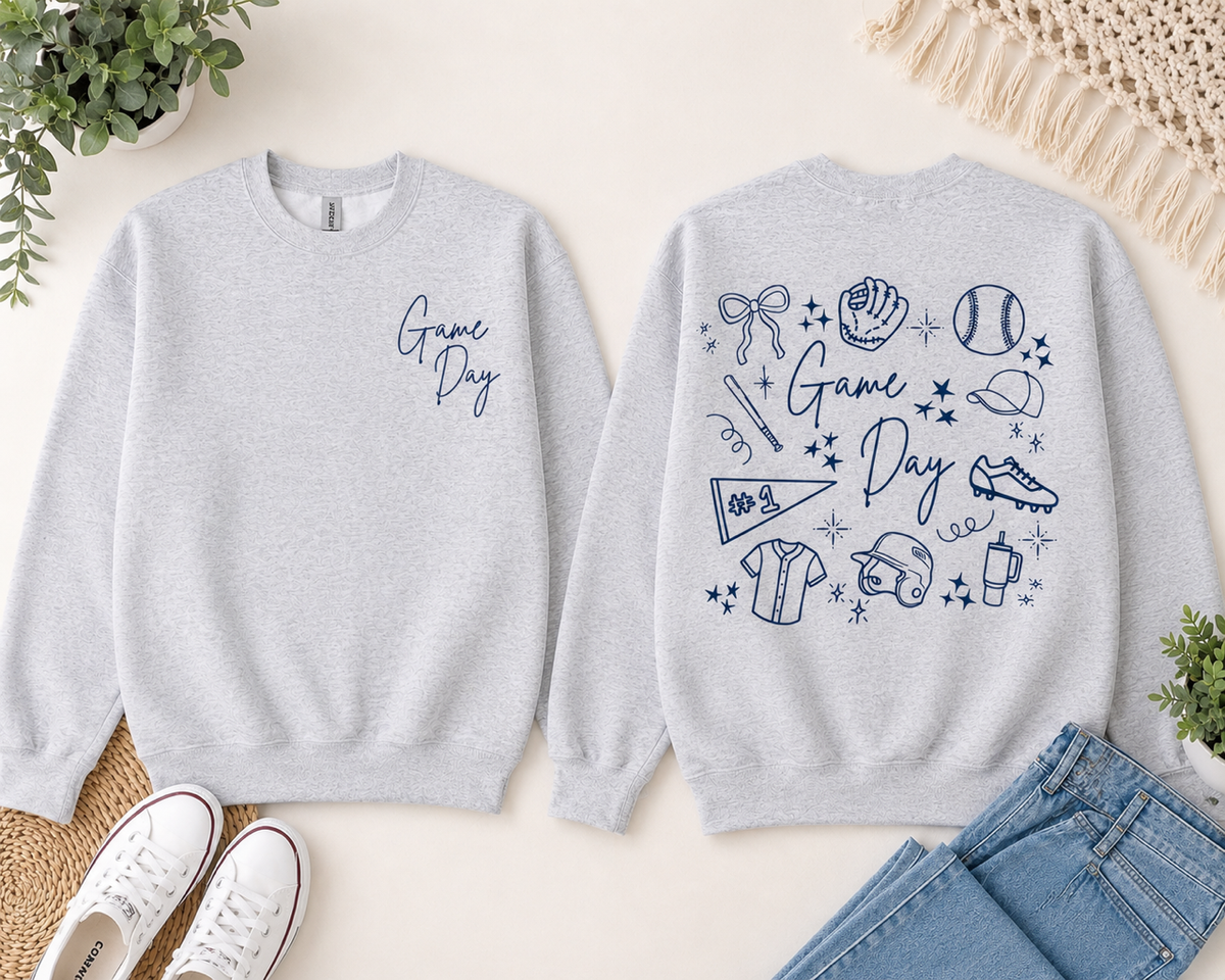 The front of a sweatshirt showing 'Game Day' written in navy blue on the front left chest on a light gray sweatshirt. The back shows a collage of softball/baseball graphics.